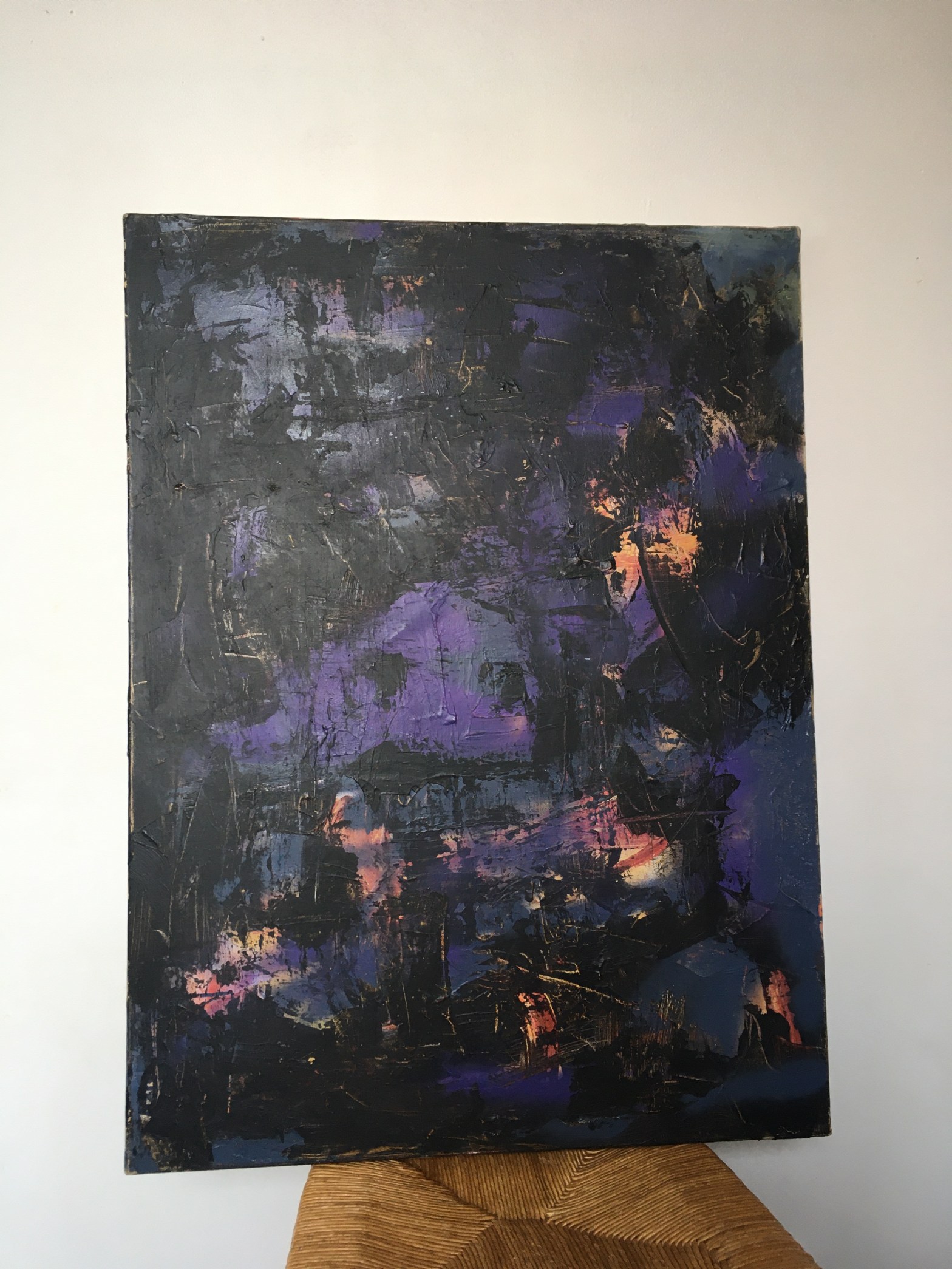 Un grand tableau posé sur une chaise, peint dans des tons violets de manière abstraite.