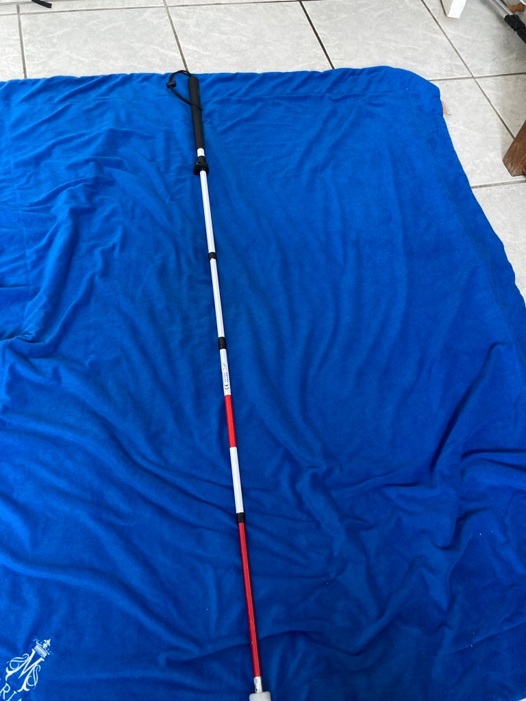 Sur une couverture bleue foncée, une canne blanche de 1m10.