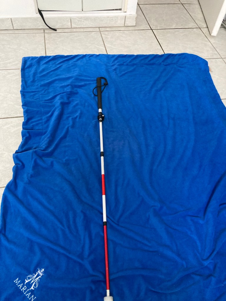 Sur une couverture bleue foncée, une canne blanche de 1m40.