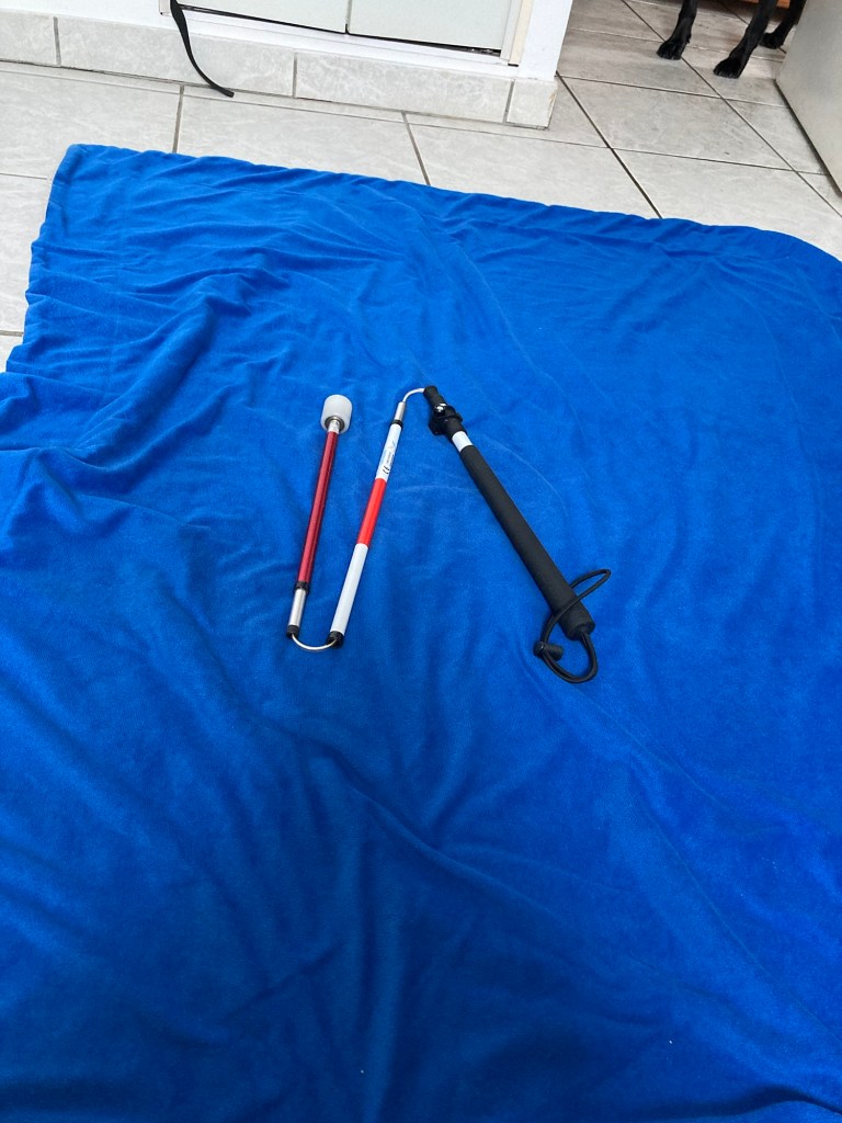 Sur une couverture bleue foncée, une canne blanche repliée formant 3 brins.