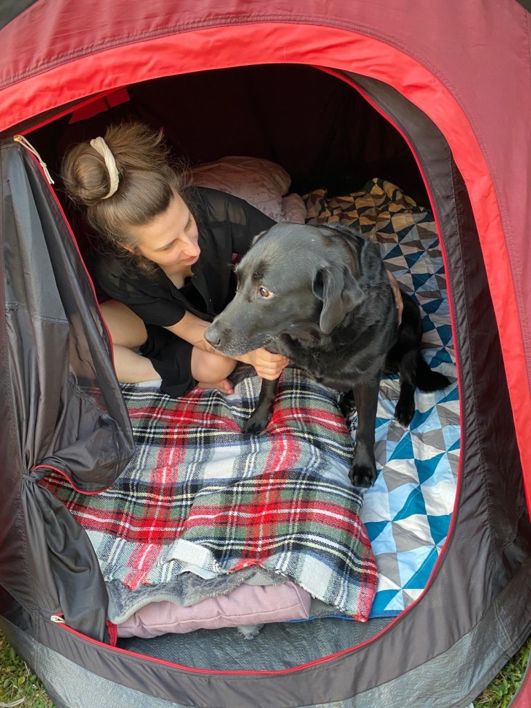 Manille, petite labrador noire, et Ilékéleur sont dans une tente. Ilékéleur est assise à gauche et sourit. Manille est assise à droite.