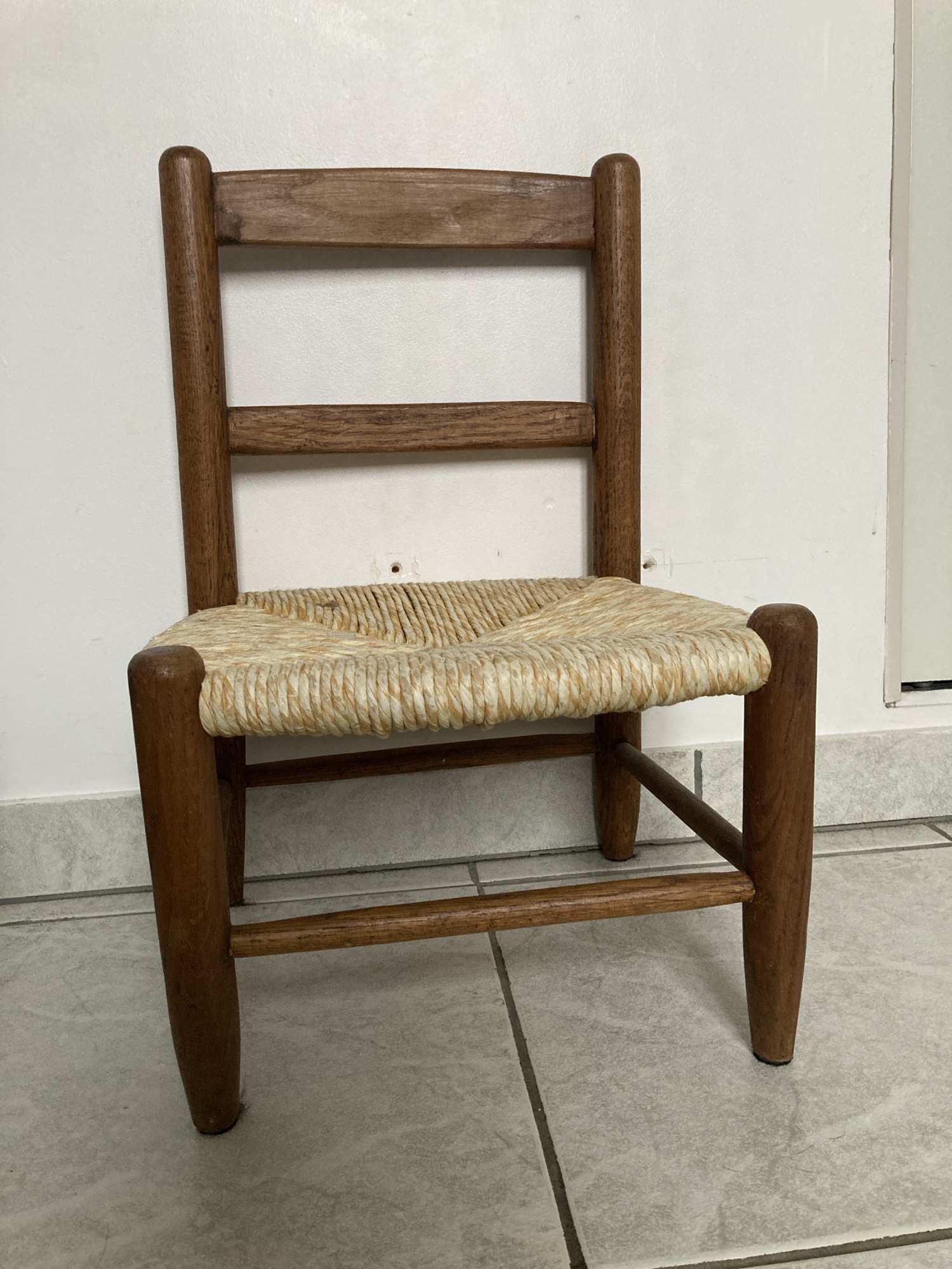 Une petite chaise pour enfant en bois avec une assise en paille tressée sur laquelle il y a une toute petije tache d’encre bleue.
