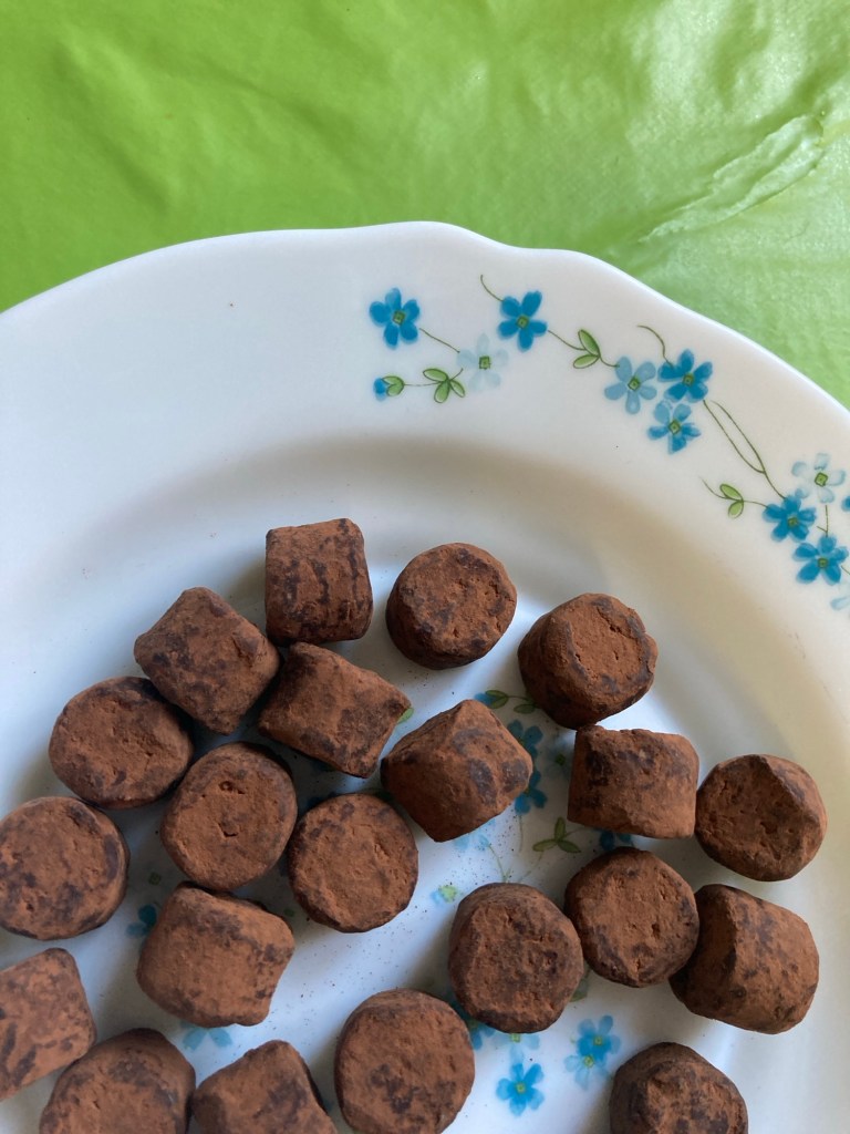 De jolies truffes au chocolat disposées sur une assiette blanche. Elles sont de forme un peu cubique et régulière.