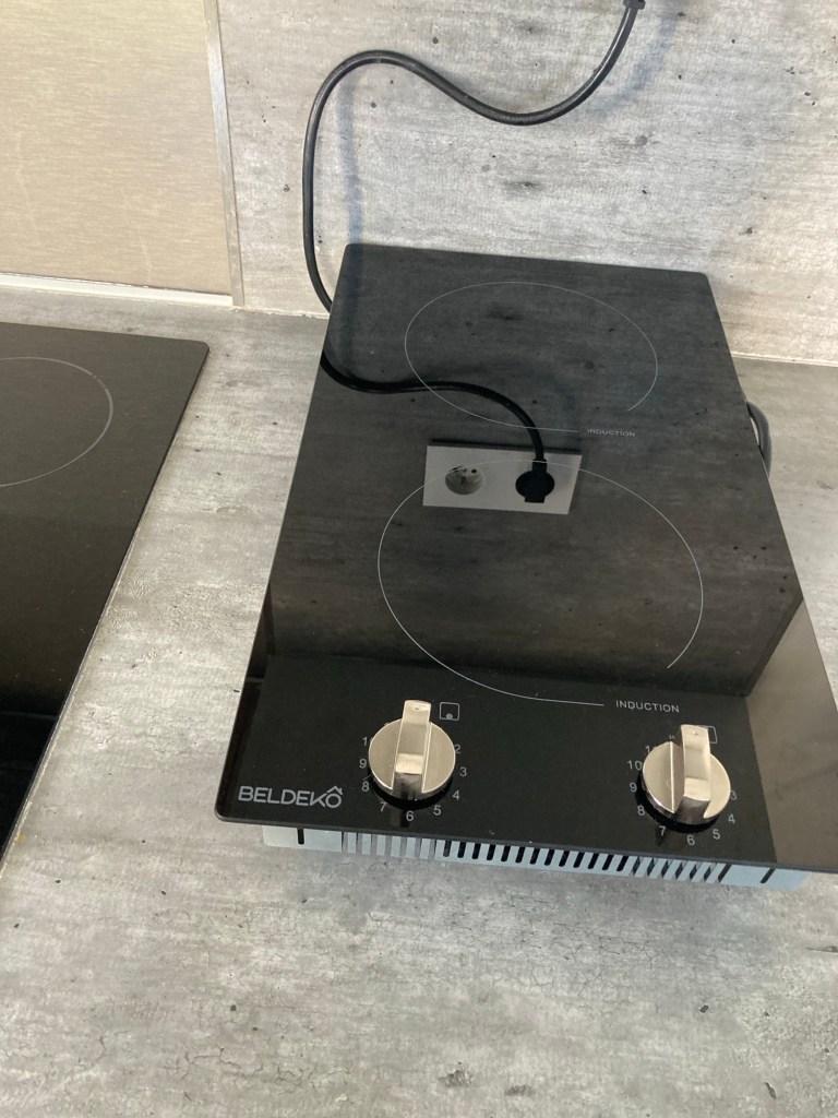 Une plaque à induction deux feux. Tout en bas de la plaque il y a deux manettes côte à côte.