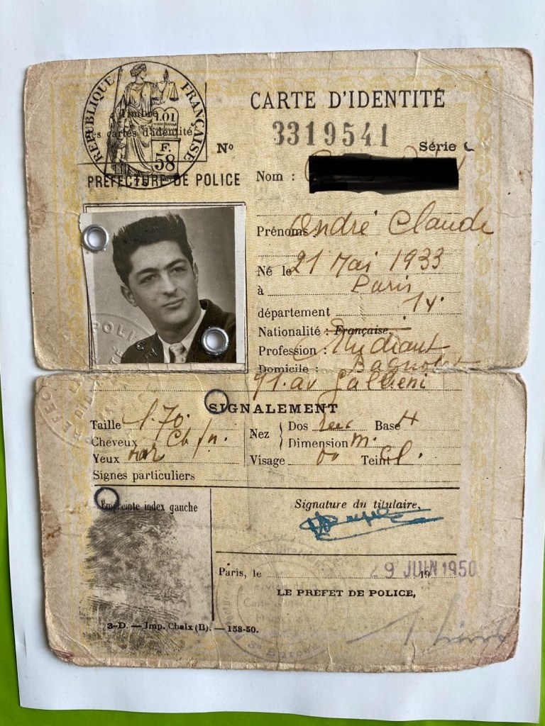Une carte d’identité de 1950 au format portrait dans un cadre photo bleu. Elle est beige clair avec un aspect vieilli, (plis et taches). L’dn-tête porte l’inscription “CARTE D’IDENTITÉ” avec un numéro de série et un cachet officiel de la Préfecture de Police. On voit un tampon rond avec l’effigie de la République Française et la mention “Sécurité Publique”. Informations personnelles : Nom et prénom : Partiellement masqués, mais on voit “André Claude”. Date et lieu de naissance : 21 mai 1933 à Paris. Nationalité : Française. Profession : Étudiant. Domicile : Indiqué mais partiellement masqué. Taille : 1,70 m, Cheveux : Châtain noir. Yeux : Marron. Visage : Ovale. Nez : Droit. Teint : Non précisé. Empreinte digitale : Une empreinte de l’index gauche est apposée en bas à gauche, ce qui était une pratique courante à l’époque. Signature : La signature du titulaire est présente en bleu, légèrement effacée avec le temps. En bas à droite, on voit une date de délivrance : 9 juin 1950, avec un tampon administratif et une signature du préfet de police. Photographie : Une photo en noir et blanc est fixée en haut à gauche avec deux rivets métalliques. Elle représente un jeune homme aux cheveux noirs, coiffés avec du volume, portant un costume et une cravate.