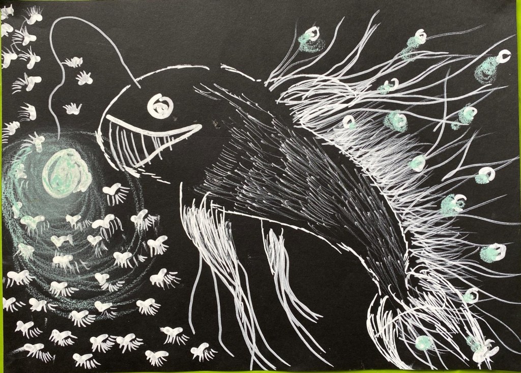 Dessin au feutre blanc et au pastel bleu sur feuille noire. Sur une bonne partie à gauche il y a un gigantesque poisson avec des espèces de filaments sur tout son dos et au niveau de ses nageoires (sur les filaments du dos il y a des « boules » de pastel bleu). Un globe lumineux est relié à sa tête (lumière bleue). Sur la partie droite tout plein de méduses semblent attirées par le globe lumineux. Les méduses ont une tête en forme de coeur. Le poisson a un grand sourire (ses dents ressemblent à des fanons). Ses yeux sont deux cercles simples très grossiers et il a l’air de regarder la personne qui l’observe.