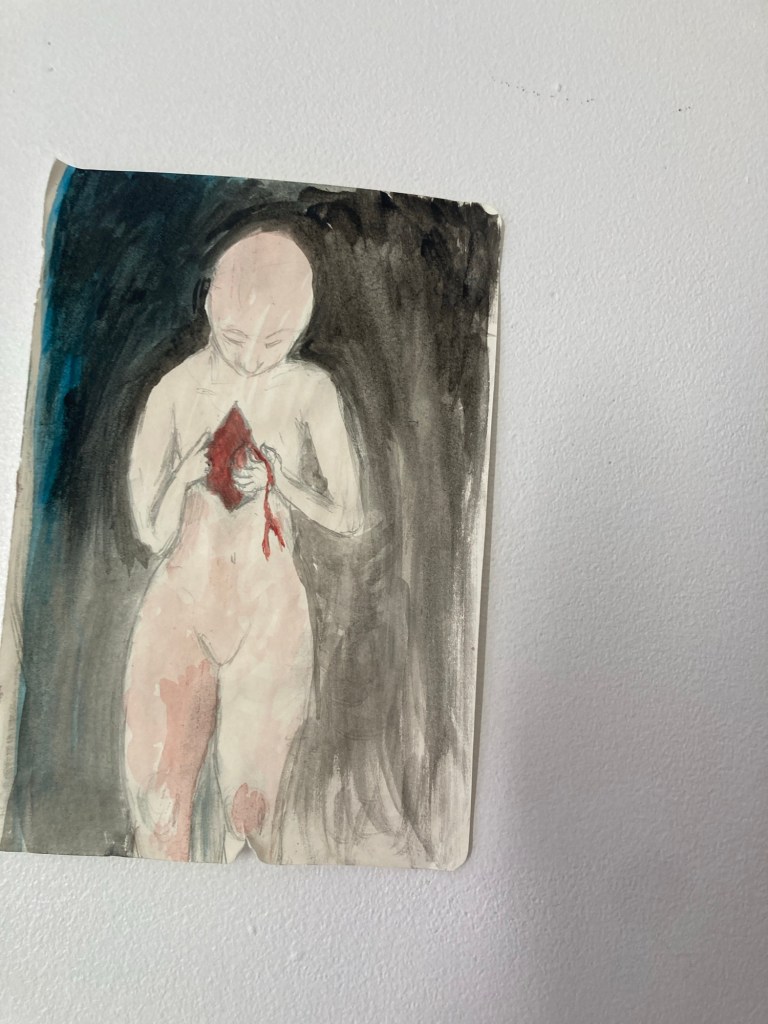 Dessin peint à l’aquarelle (mais couleurs très sombres et peinture assez homogène). Sur un fond noir un personnage à la peau beige. Le personnage n’a pas de vêtement. Il est coupé un peu en-dessous des genoux. Il est chauve et semble regarder dans un petit espace au niveau de sa poitrine (au milieu) où il passe ses doigts. Un peu de sang lui coule sur la main. Il n’a pas de sexe mais une morphologie plutôt féminine avec une taille marquée.