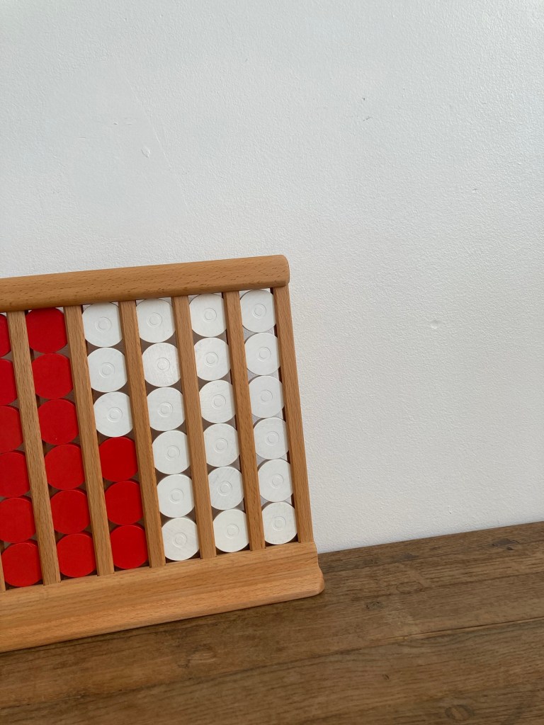 Un jeu de Puissance 4 tout en bois. Visuellement les jetons sont rouges et blancs et sont aussi distinguables au toucher. Les jetons sont disposés dans le « plateau » qui est à la verticale.