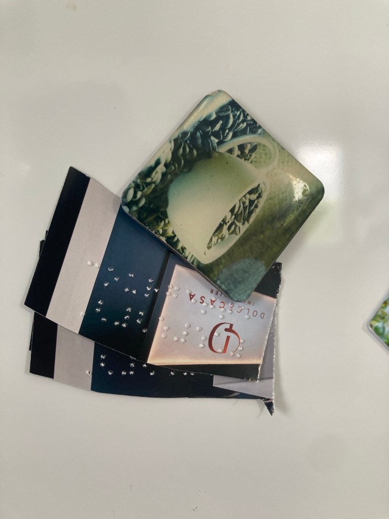 Sur un frigo blanc un aimant accroche plusieurs petits bouts de papier (découpés dans des prospectus publicitaires) sur lesquels il y a du braille.