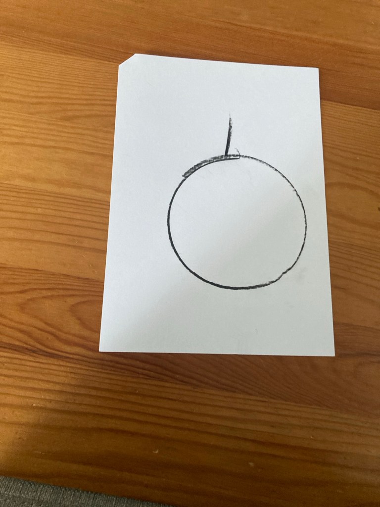 Sur une feuille de papier blanche a été dessiné au crayon noir un cercle avec une ligne verticale en haut de celui-ci.