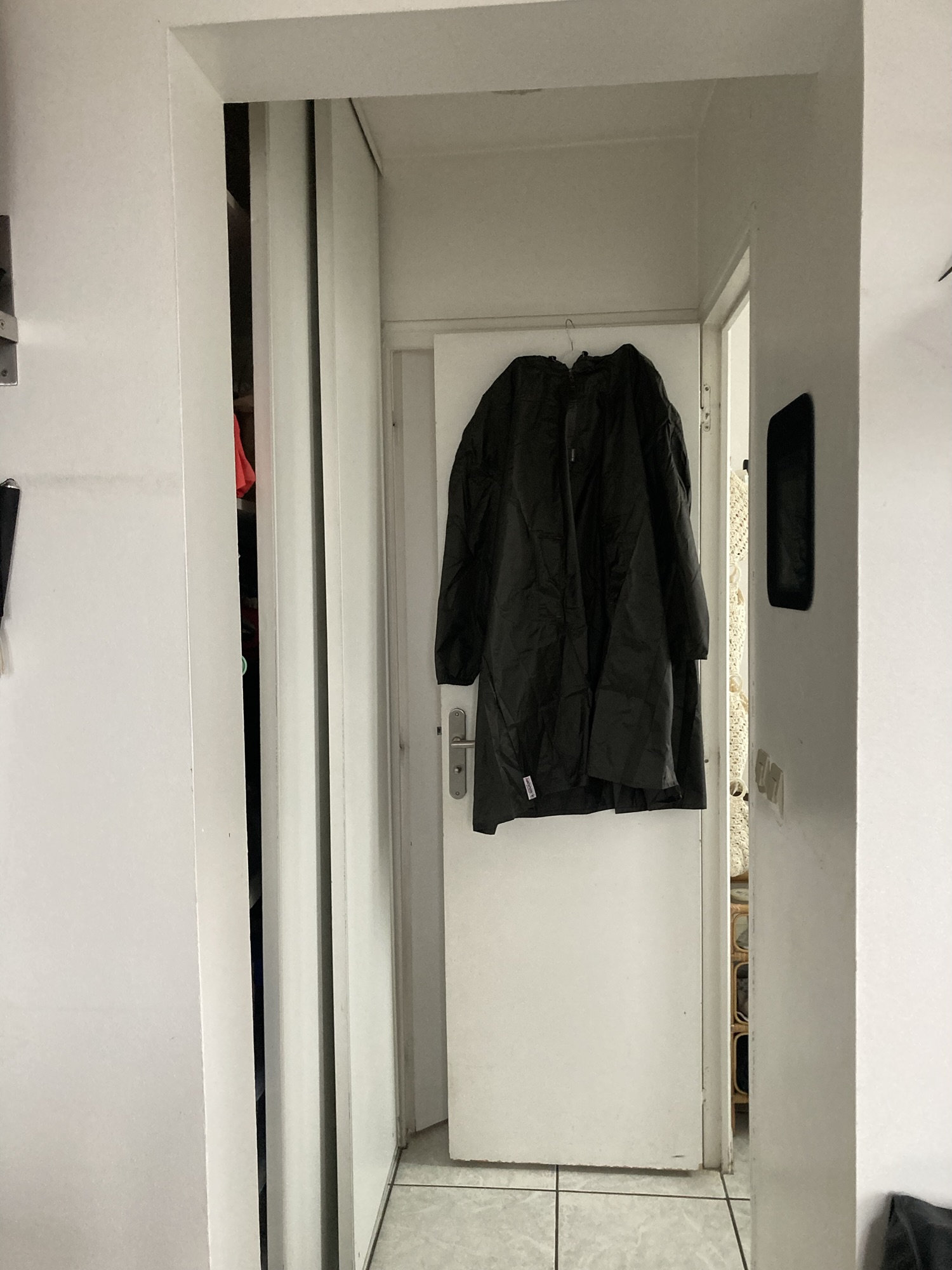 Suspendu à une porte blanche, un grand manteau de pluie noir.